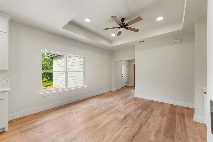 Spacious room featuring wood-finish flooring, a tray ceiling with recessed lighting, and a modern ceiling fan