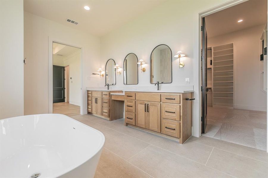 Bathroom with a freestanding bath, double vanity, recessed lighting, light tile patterned floors, and a walk in closet