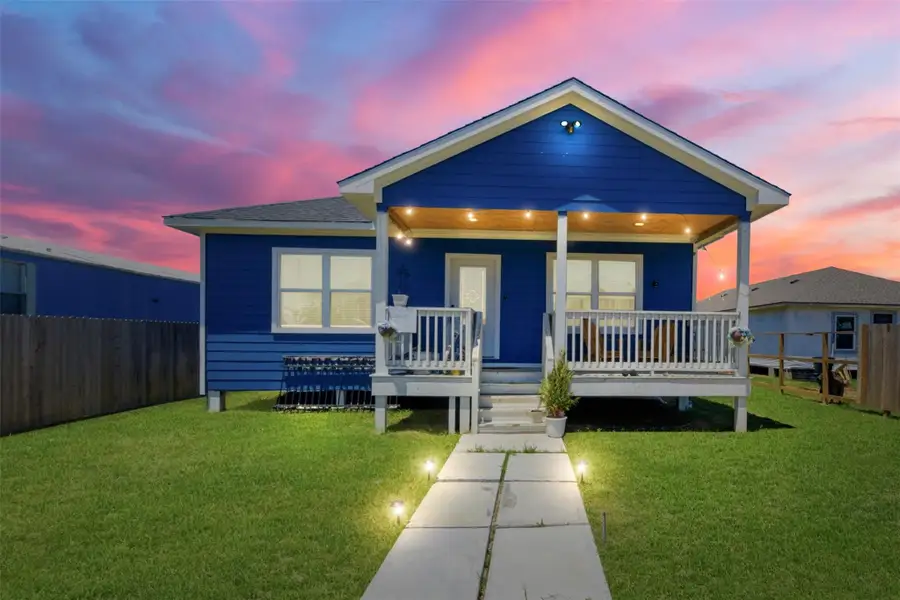 Charming blue bungalow with a welcoming front porch, set against a vibrant sunset sky. With pathway lighting to enhance its curb appeal.