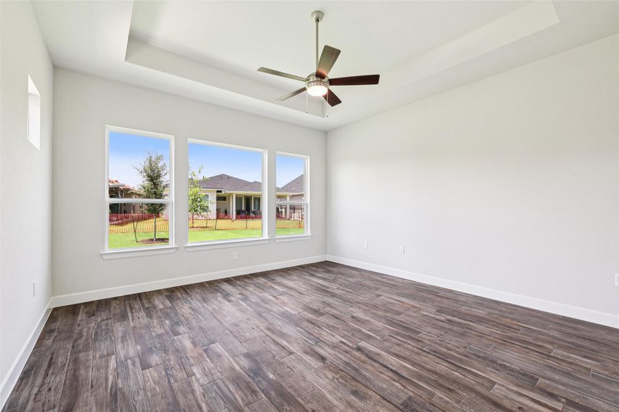 Empty room featuring dark wood-type flooring, a ceiling fan, and a raised ceiling