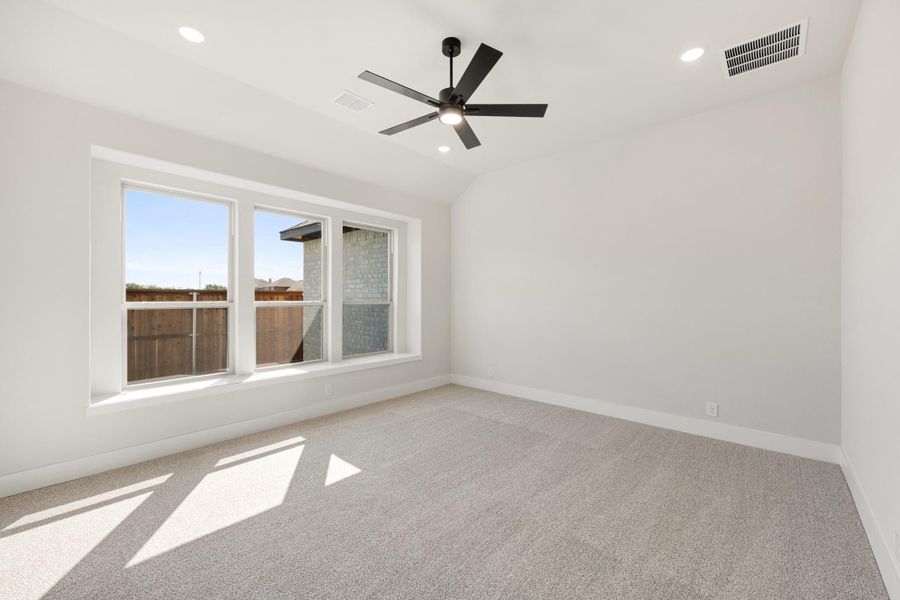 Empty bedroom with vaulted ceiling, black ceiling fan, carpet flooring, and large windows with natural light