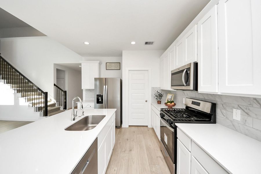 This modern kitchen features sleek white cabinetry, stainless steel appliances, and a spacious island with a farm sink. It has a bright, open layout connecting the living room and dining room, enhancing the contemporary feel.
