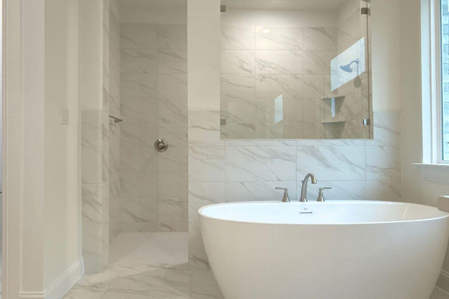 Full bath featuring a freestanding tub, tile walls, tiled shower, and light marble finish floors