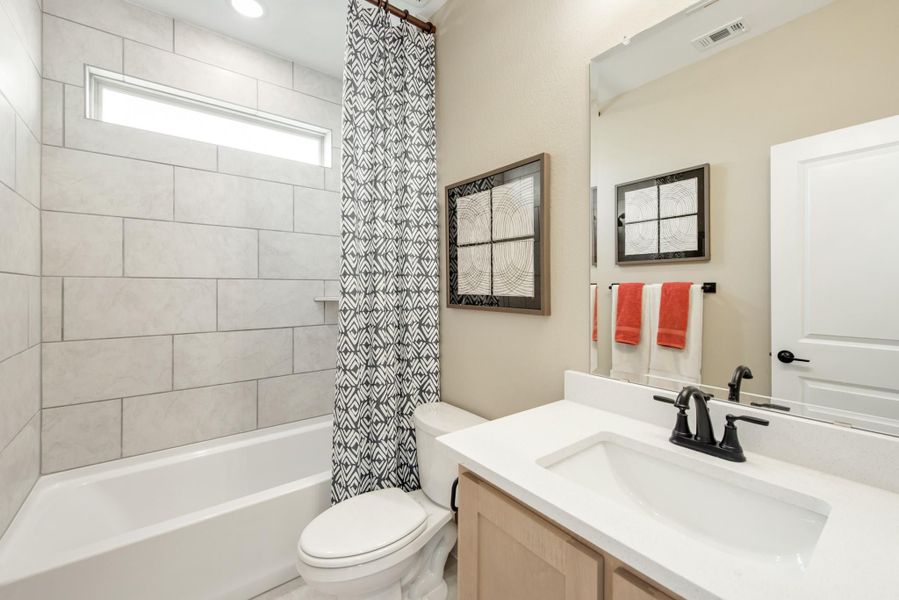 Bathroom with tiled tub and shower, white vanity with dark faucet, and patterned shower curtain Bathroom with tiled tub and shower, white vanity with dark faucet, and patterned shower curtain