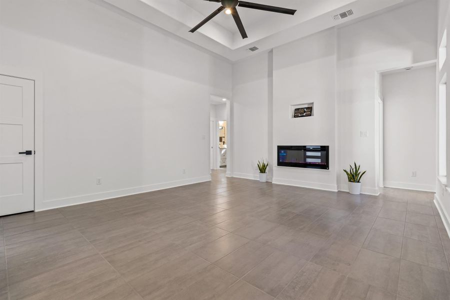 Unfurnished living room featuring a high ceiling, a glass covered fireplace, and a ceiling fan
