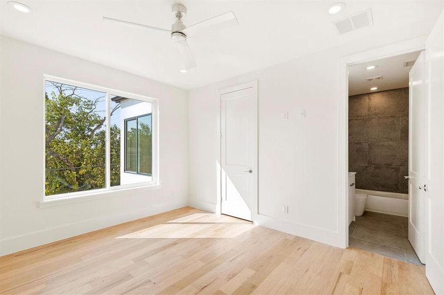 Unfurnished bedroom featuring light hardwood / wood-style floors, ensuite bathroom, multiple windows, and ceiling fan