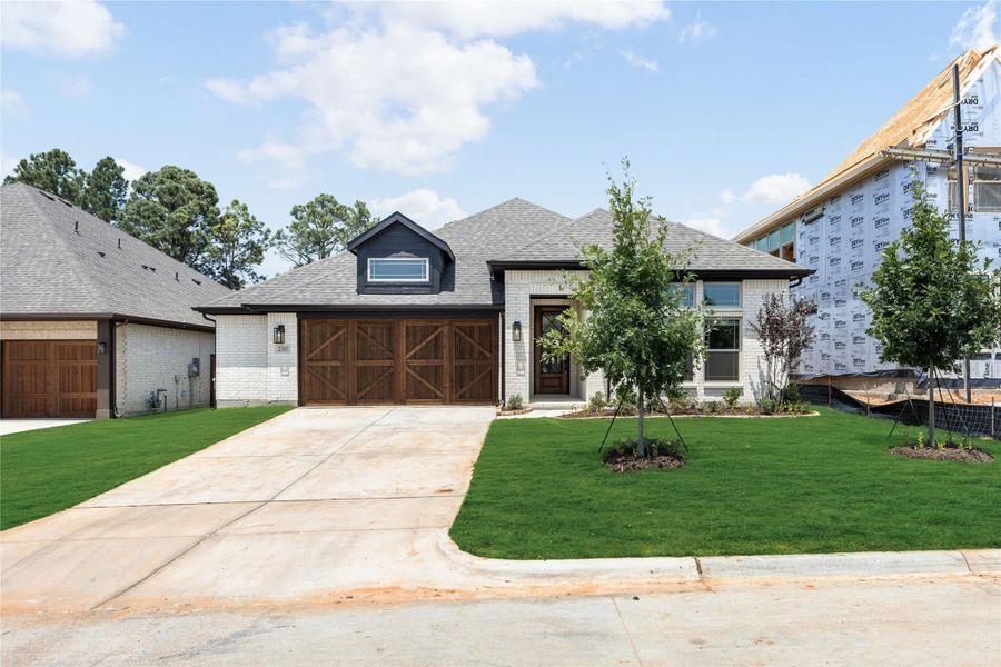 Single-story home with white brick exterior, wood garage doors, and manicured front lawn