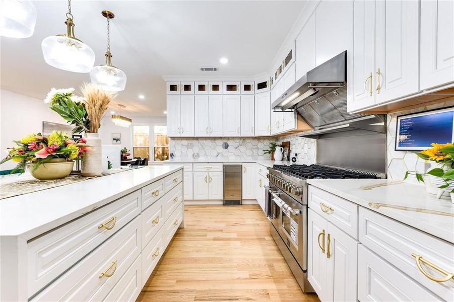 Kitchen with range hood, decorative light fixtures, white cabinets, decorative backsplash, and range with two ovens