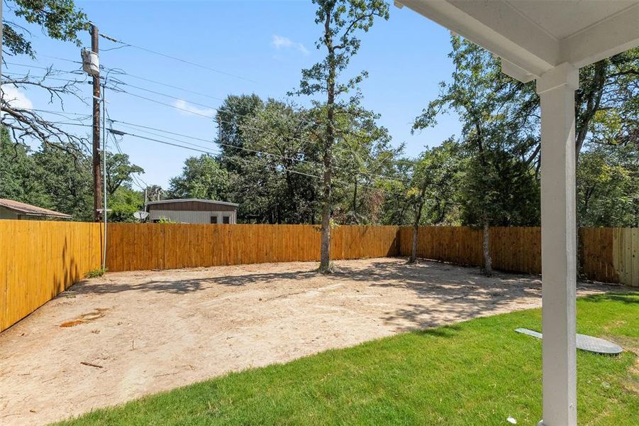 Expansive backyard featuring a new wood privacy fence, mature trees, and a covered patio area with a white column