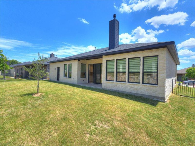 Rear exterior featuring a spacious lawn, light-colored brick siding, and a covered patio