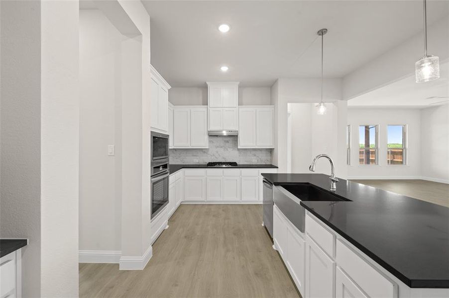 Kitchen featuring appliances with stainless steel finishes, dark countertops, light wood-style floors, decorative backsplash, and recessed lighting