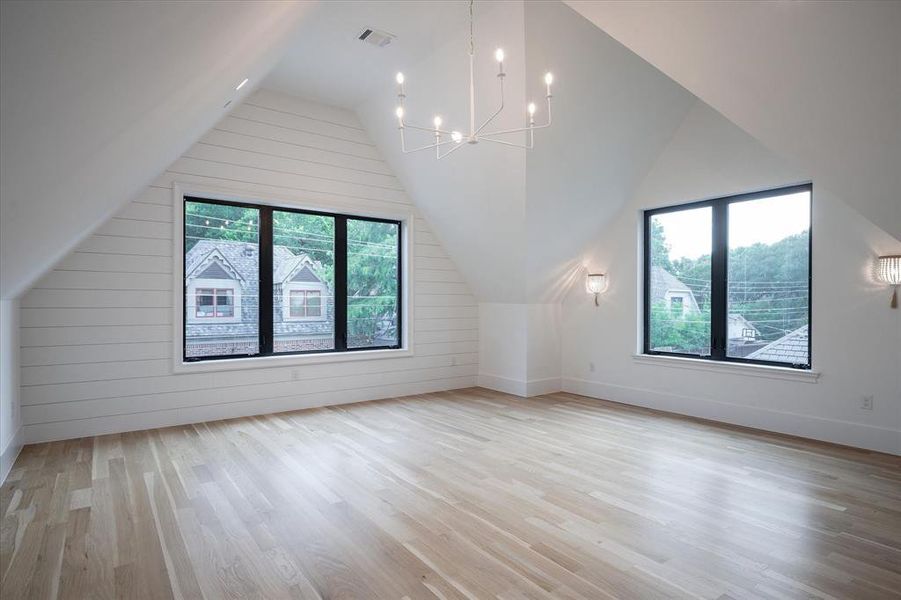 Bonus room with lofted ceiling, a chandelier, wood walls, and light hardwood / wood-style floors