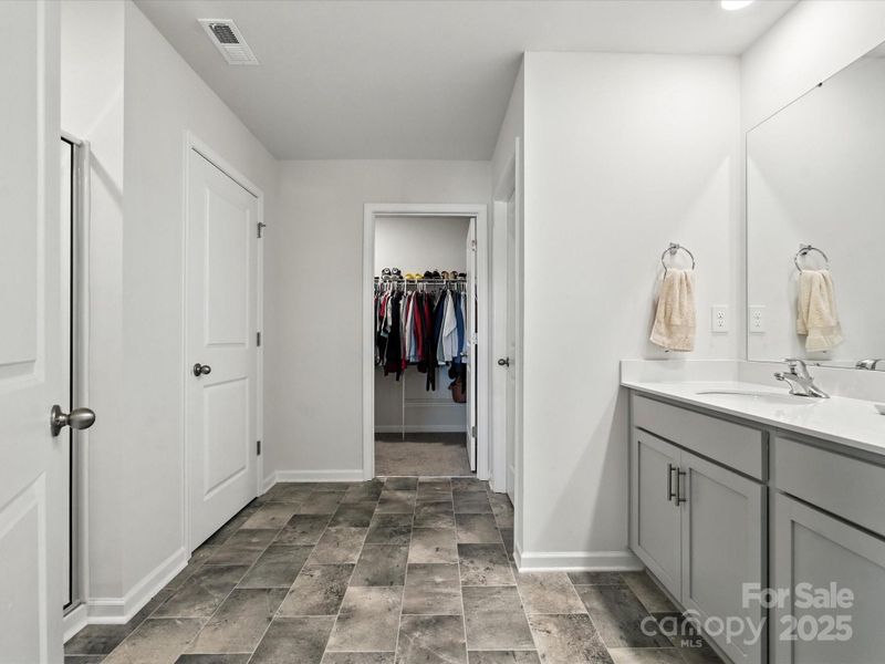 Complete primary bathroom with dual vanities, separate shower, and walk-in closet access. Gray and white color scheme with tile flooring creates modern, spa-like atmosphere.