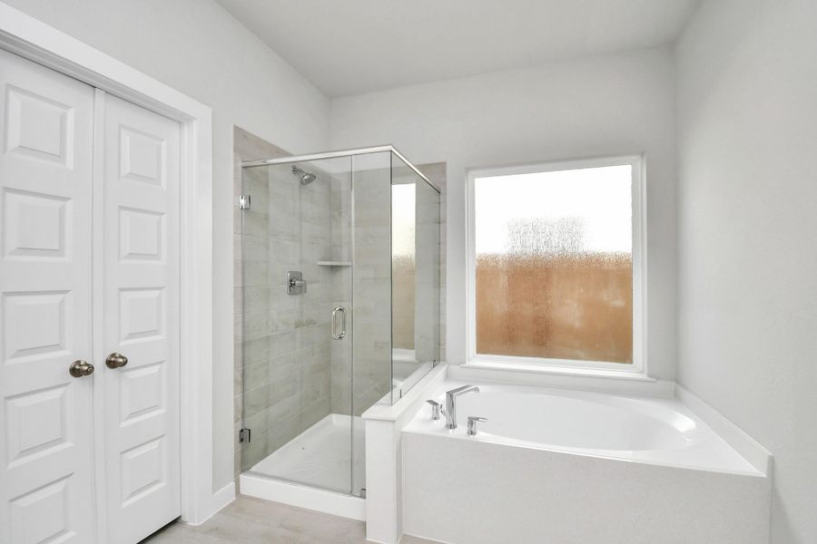 Indulge in a spa-like retreat within the confines of this primary bathroom. Delight in a spacious walk-in shower enveloped in stylish tile surround and unwind in a separate garden tub adorned with custom detailing. Sample photo of completed home with similar floor plan. Actual colors and selections may vary.