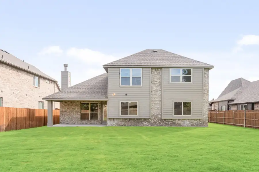 Two-story home with brick and siding exterior, covered patio, and fenced backyard with green lawn