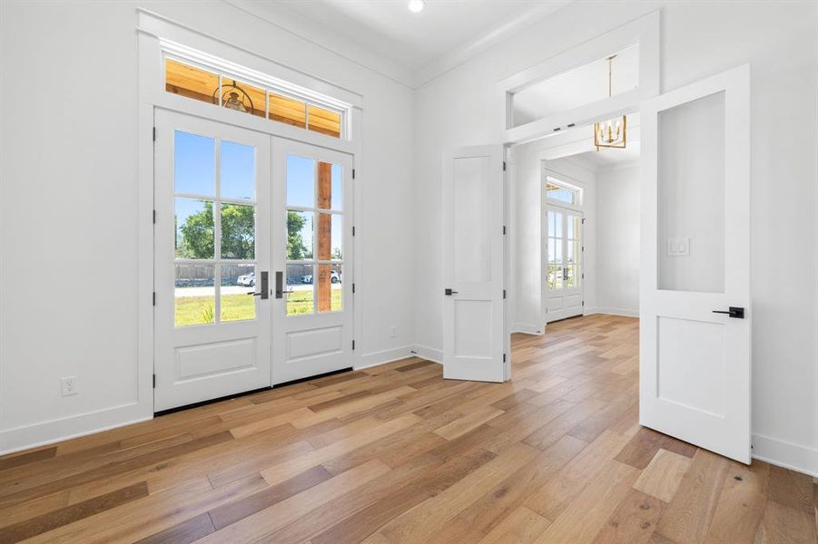 Foyer entrance with french doors, light hardwood / wood-style floors, an inviting chandelier, and crown molding