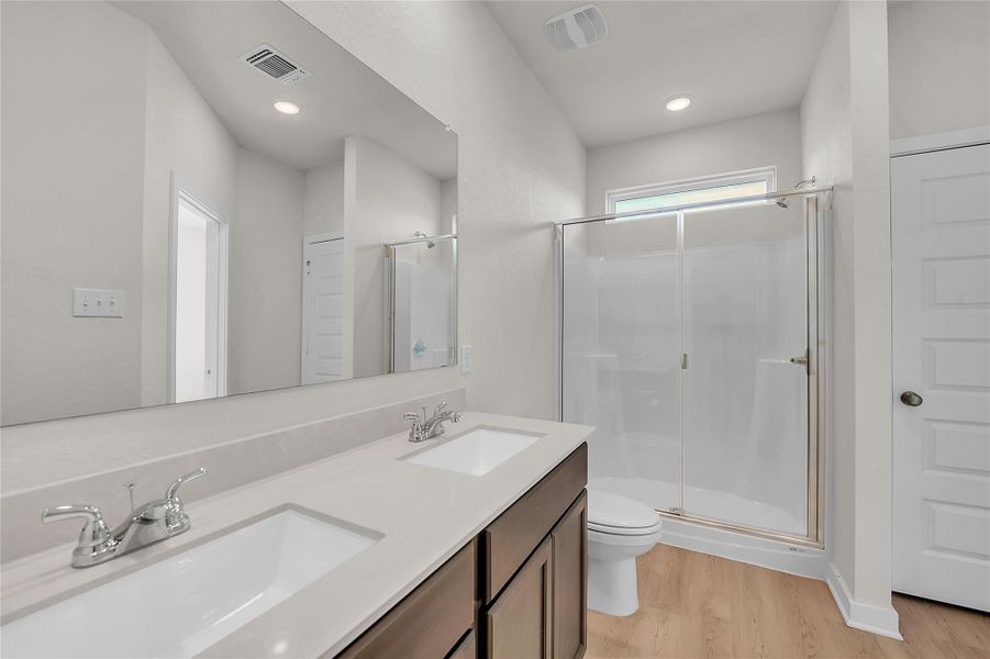 Bathroom with double vanity, a shower stall, and light wood-type flooring