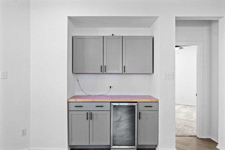 Indoor bar with gray cabinets, wine cooler, wood counters, and light wood-style floors