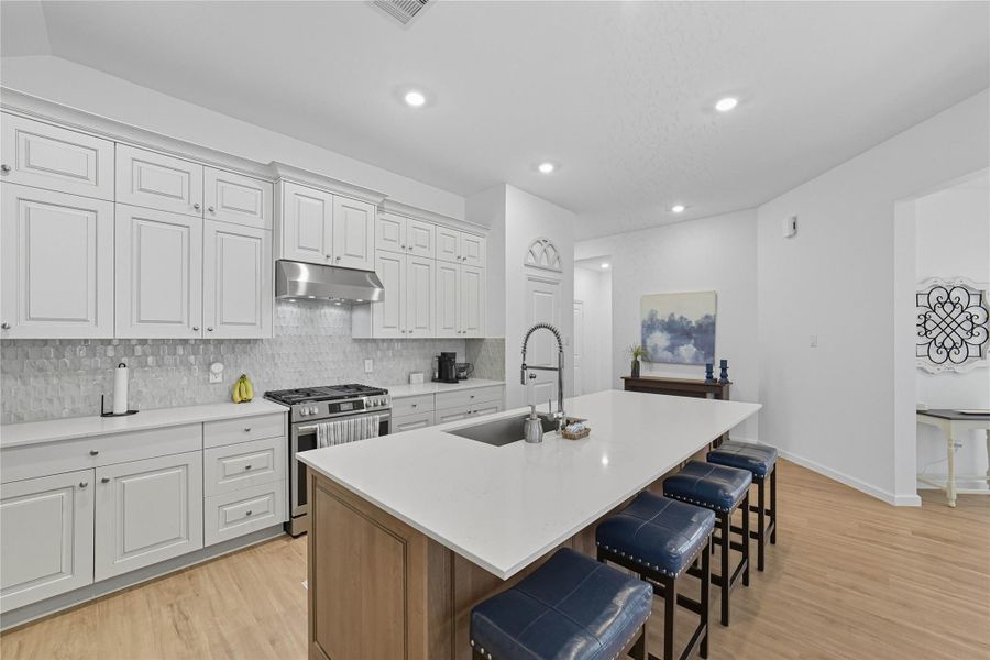 This modern kitchen features sleek white cabinetry, a stainless-steel range hood, and a spacious island with seating. This modern kitchen features sleek white cabinetry, a stainless-steel range hood, and a spacious island with seating.