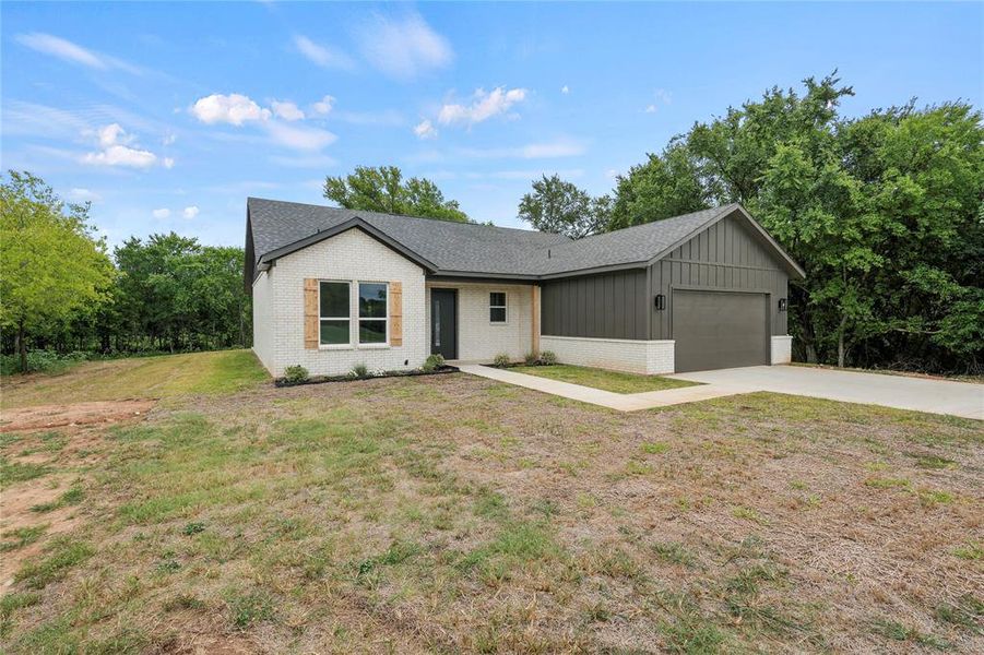 Ranch-style house with brick siding, an attached garage, a shingled roof, concrete driveway, and board and batten siding