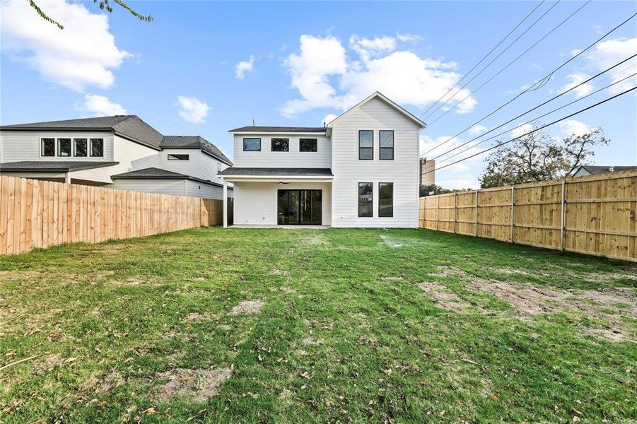 Spacious backyard featuring a new wooden privacy fence, a verdant lawn, and a modern white exterior with black-framed windows and sliding glass doors