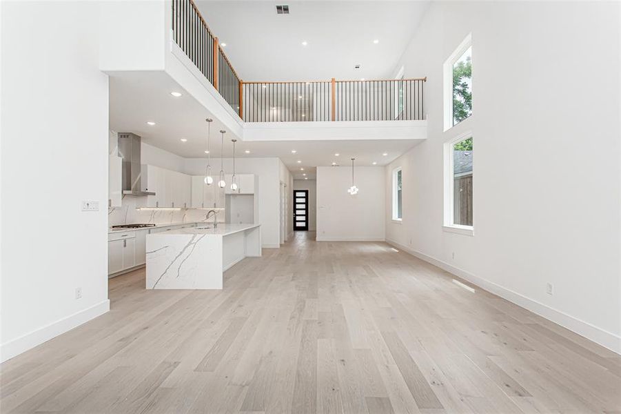 Unfurnished living room featuring a high ceiling, a sink, light wood-style flooring, baseboards, and recessed lighting