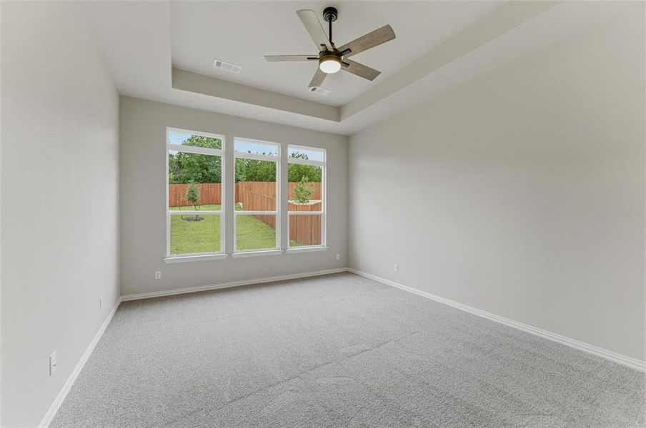 Room featuring a tray ceiling with a ceiling fan, light gray wall paint, and gray carpet