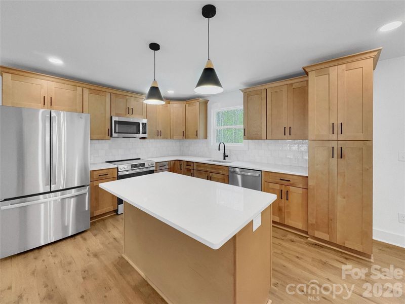 Beautiful kitchen with natural wood colored cabinets, quartz counters, tile backsplash, and stainless steel appliances Beautiful kitchen with natural wood colored cabinets, quartz counters, tile backsplash, and stainless steel appliances