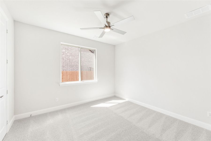 Empty bedroom with light gray carpet, ceiling fan, and single window with backyard view Empty bedroom with light gray carpet, ceiling fan, and single window with backyard view