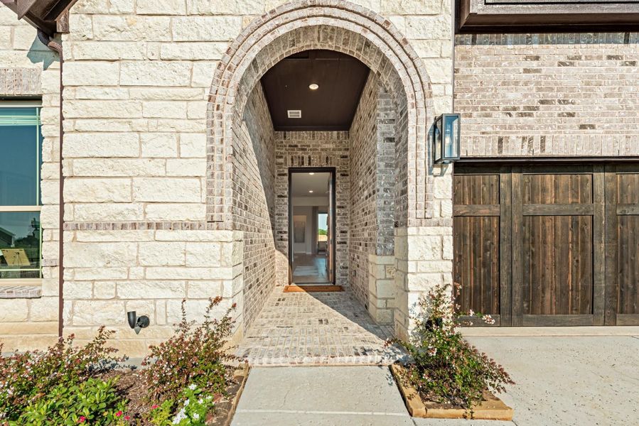 Home entrance with stone and brick arched entryway, brick walkway, and wood garage door nearby Home entrance with stone and brick arched entryway, brick walkway, and wood garage door nearby