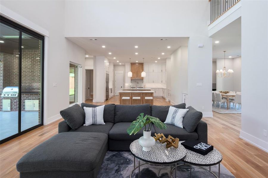 Living room featuring sink, light hardwood / wood-style floors, a chandelier, and a towering ceiling