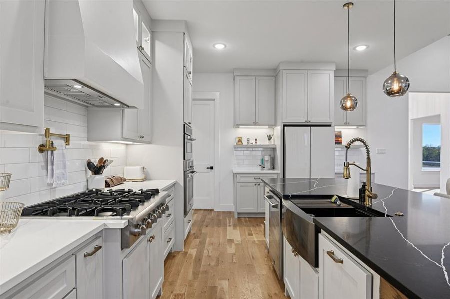 Kitchen featuring dark stone countertops, hanging light fixtures, tasteful backsplash, custom range hood, and light wood finished floors Kitchen featuring dark stone countertops, hanging light fixtures, tasteful backsplash, custom range hood, and light wood finished floors