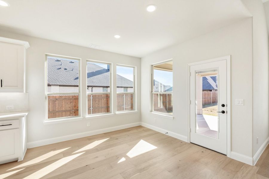 Bright dining area with light wood floors, three windows, and a glass back door leading to a patio