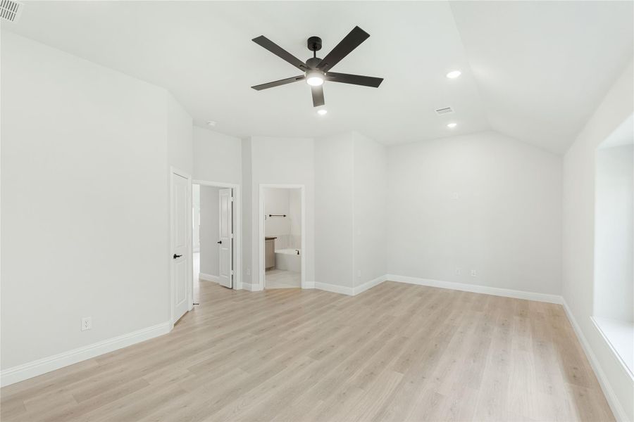 Empty bedroom with light wood floors, ceiling fan, and open ensuite bathroom doorway