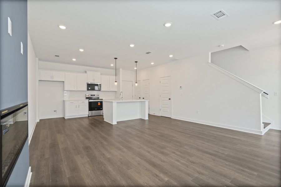 Open concept living space featuring wood-finish flooring, recessed lighting, and a modern kitchen with white cabinetry and stainless steel appliances