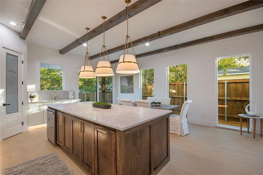 Kitchen with light wood finished floors, decorative light fixtures, light stone counters, dark brown cabinets, and beamed ceiling