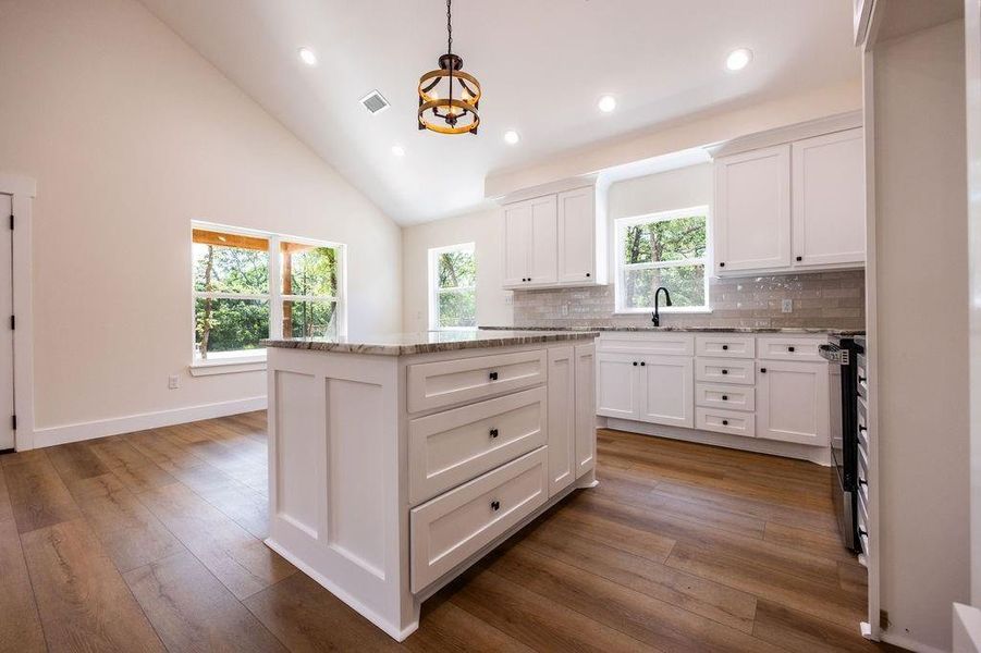 Kitchen featuring light stone counters, white cabinets, high vaulted ceiling, black range oven, and a kitchen island