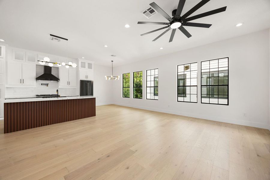 A wider view showcases the generous living area, large ceiling fan, abundant windows, and seamless connection to the kitchen.
