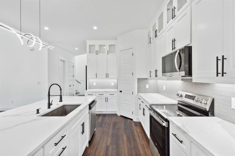 Kitchen with stainless steel appliances, dark wood-type flooring, sink, pendant lighting, and white cabinetry