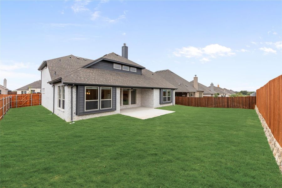 Rear exterior of brick and gray siding home with large fenced backyard, concrete patio, and green lawn
