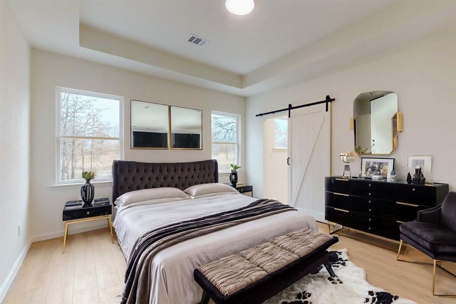 Bedroom with light wood finished floors, a raised ceiling, and a barn door