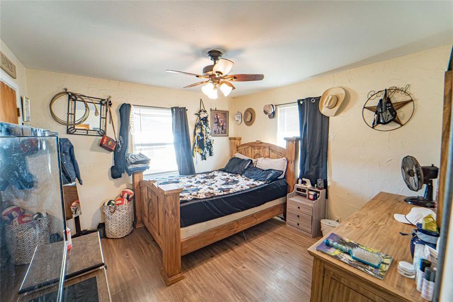 Bedroom with a textured wall, laminate flooring multiple windows, and a ceiling fan