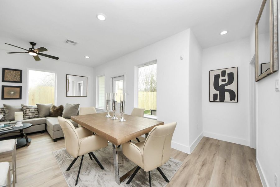 Bright and modern open-concept living and dining area with light wood flooring, neutral tones, and contemporary decor. A ceiling fan and large windows provide ample light. There's a cozy sectional sofa and a stylish dining table with beige chairs. Bright and modern open-concept living and dining area with light wood flooring, neutral tones, and contemporary decor. A ceiling fan and large windows provide ample light. There's a cozy sectional sofa and a stylish dining table with beige chairs.