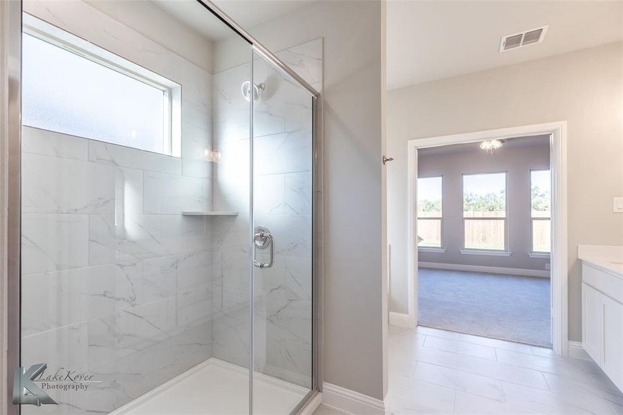 Full bathroom featuring plenty of natural light, a marble finish shower, vanity, and light marble style patterned flooring