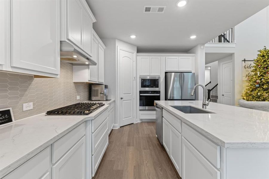 Kitchen with light stone countertops, white cabinets, dark wood-style floors, stainless steel appliances, and a kitchen island with sink Kitchen with light stone countertops, white cabinets, dark wood-style floors, stainless steel appliances, and a kitchen island with sink