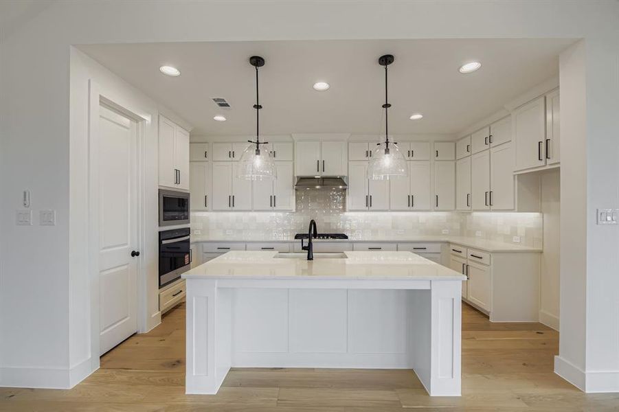 Kitchen featuring white cabinets, hanging light fixtures, tasteful backsplash, stainless steel appliances, and light stone countertops Kitchen featuring white cabinets, hanging light fixtures, tasteful backsplash, stainless steel appliances, and light stone countertops