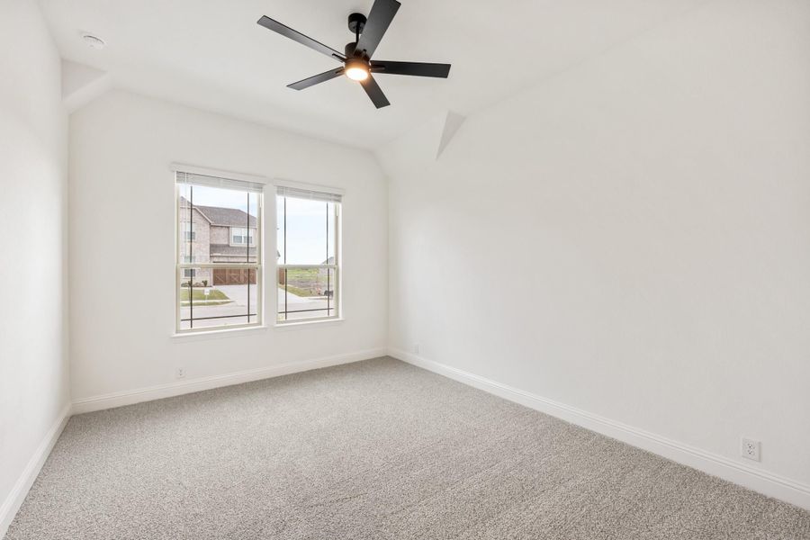 Empty bedroom with carpet flooring, black ceiling fan, vaulted ceiling, and double window with neighborhood view