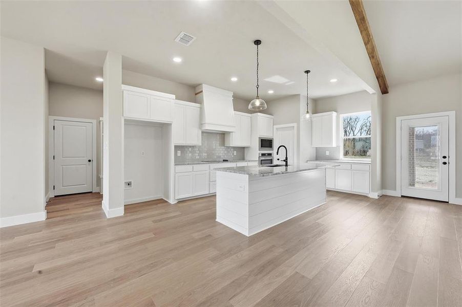 Kitchen featuring white cabinets, decorative light fixtures, tasteful backsplash, light stone counters, and beam ceiling