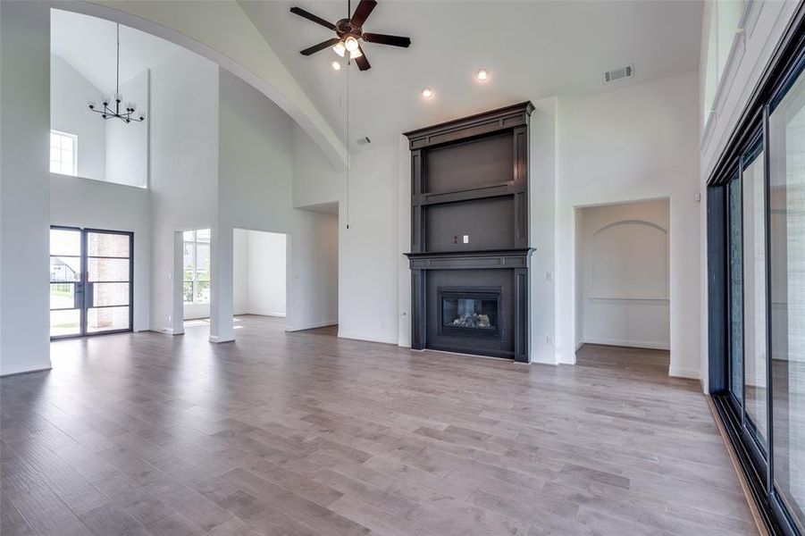 Unfurnished living room with high vaulted ceiling, ceiling fan with notable chandelier, and hardwood / wood-style floors