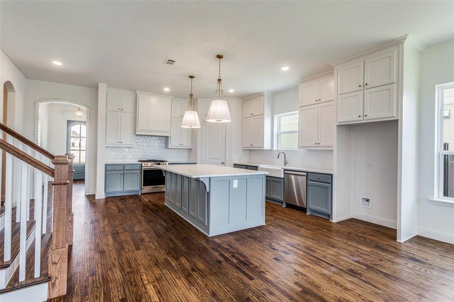 Kitchen featuring dark wood-type flooring, a kitchen island, appliances with stainless steel finishes, pendant lighting, and a healthy amount of sunlight